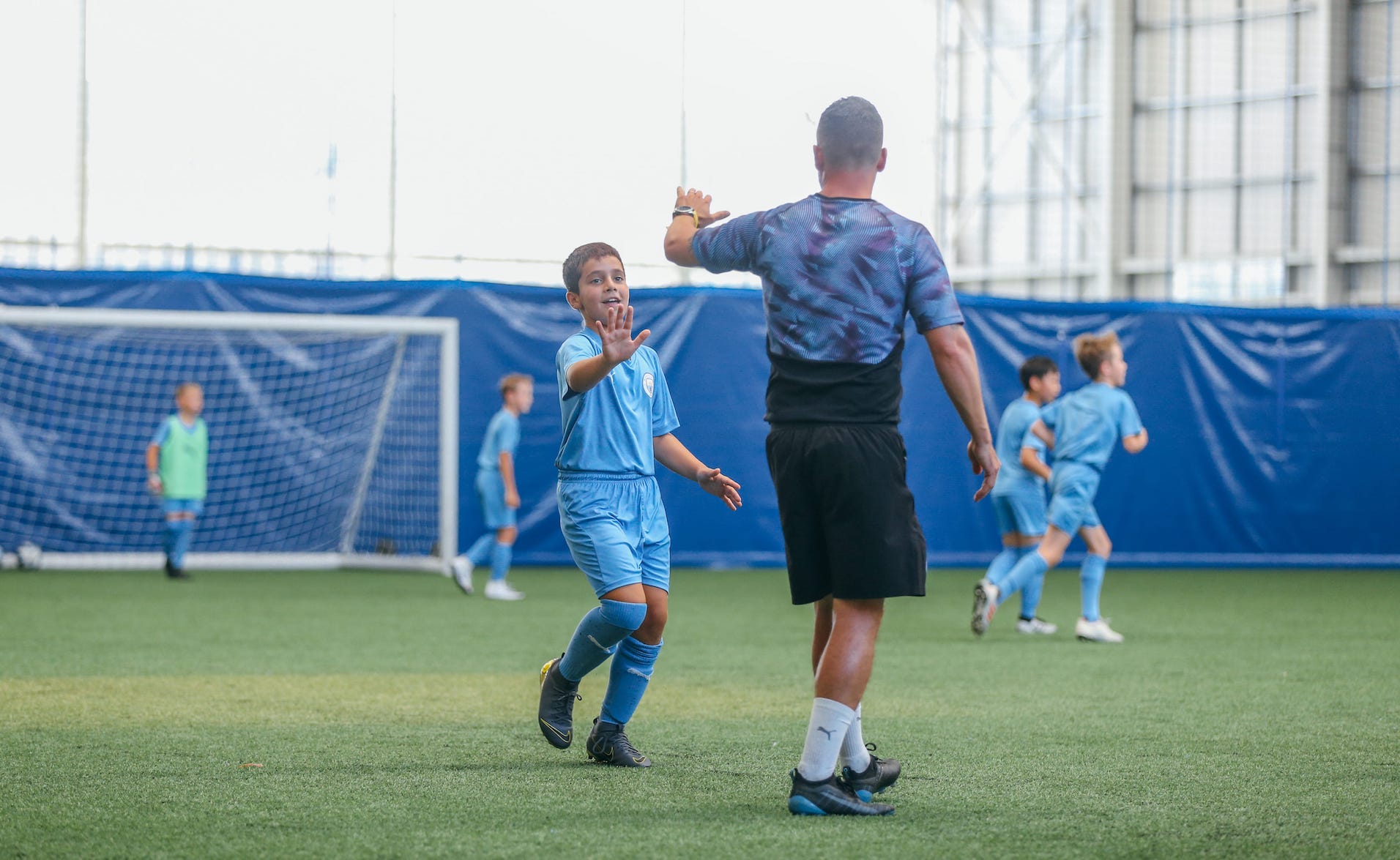 A young boy high fiving his football coach at Manchester City Football School.