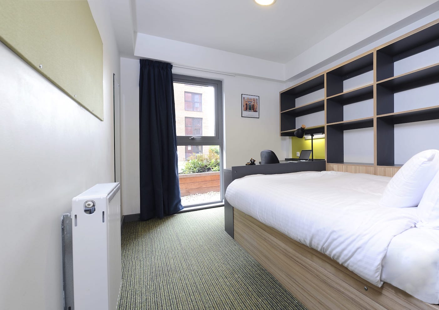 A typical bedroom at Manchester City’s residential football camp in the UK. The bedroom has a window, a double bed with white bedding and a desk.
