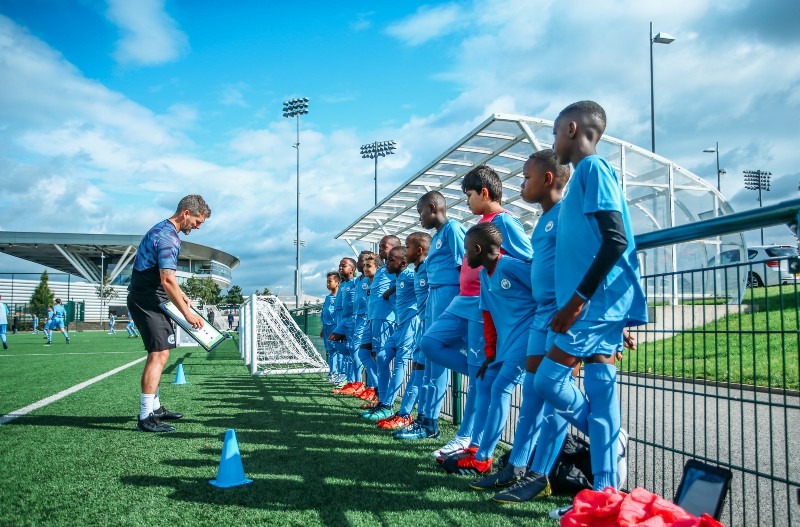A male coach at Manchester City Football School, with students.