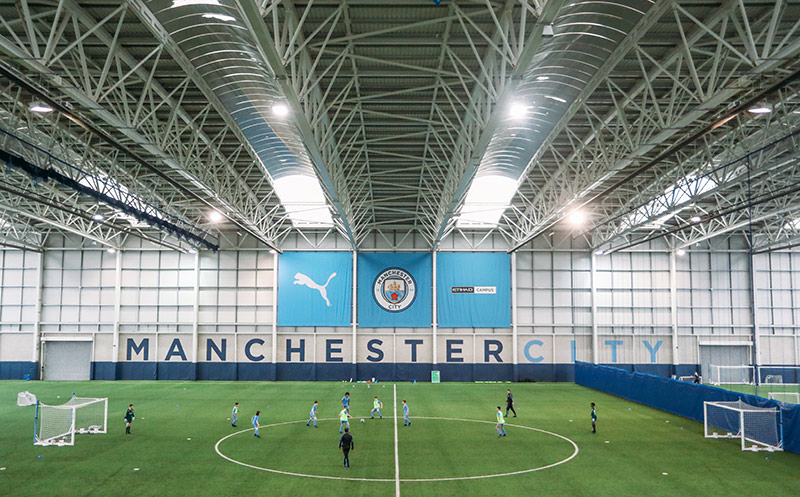 A boys football team playing at the indoor pitch at Manchester City Football School.